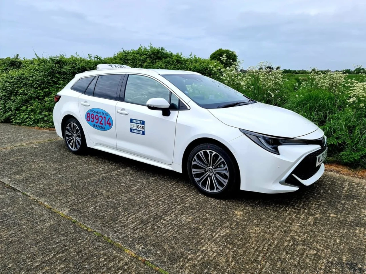 White Cuckmere Taxis Toyota Corolla Estate with company door logo and taxi roof sign